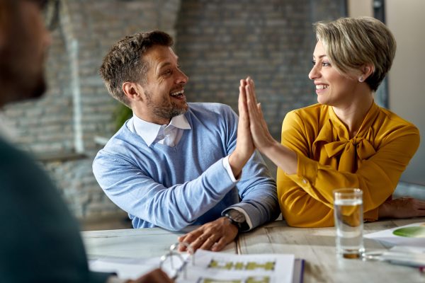 Happy couple celebrating and giving high-five to each other while being on a meeting with real estate agent.