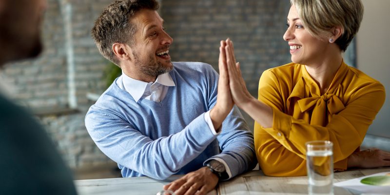 Happy couple celebrating and giving high-five to each other while being on a meeting with real estate agent.