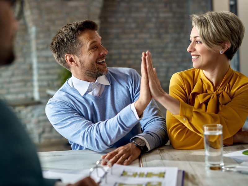 Happy couple celebrating and giving high-five to each other while being on a meeting with real estate agent.